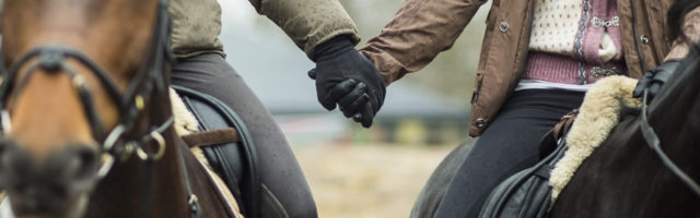 Low section of couple holding hands while riding horses 